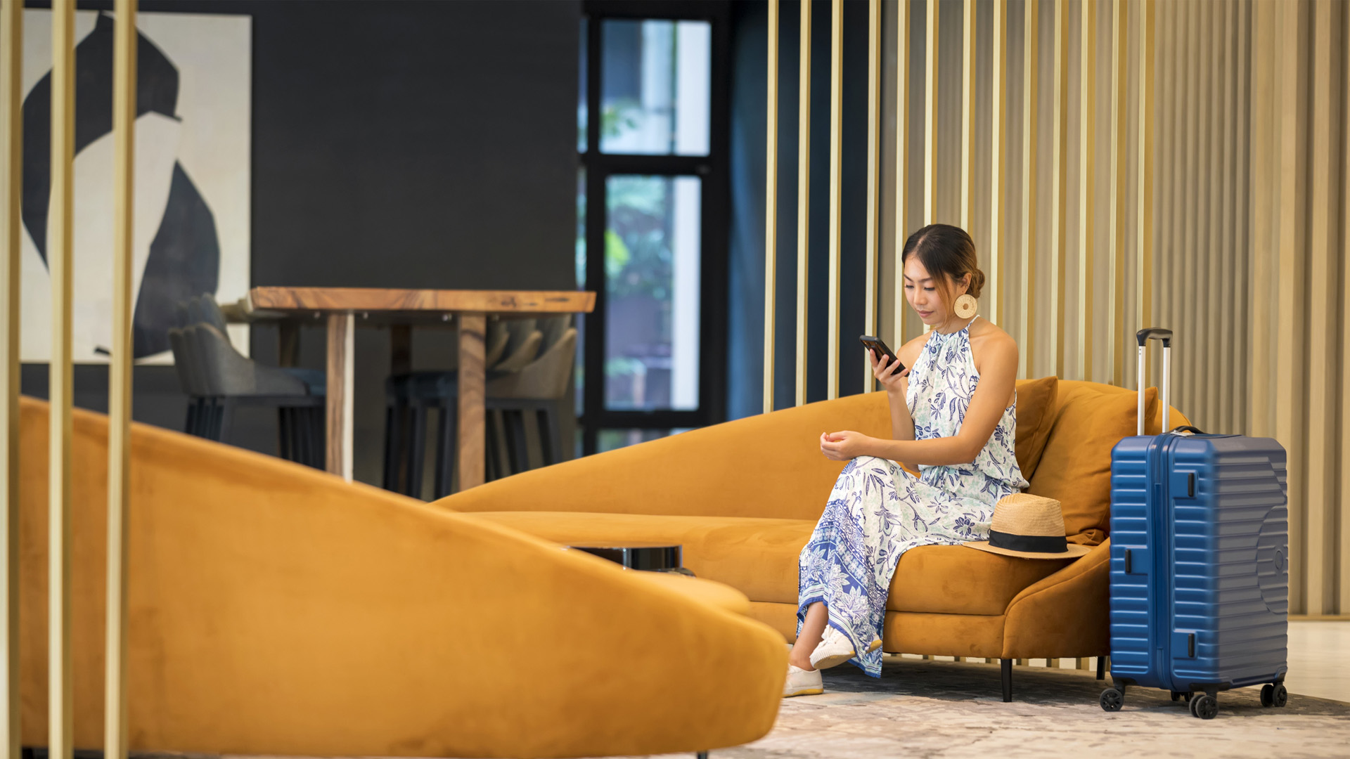 Woman sitting with luggage in hotel lobby looking at mobile phone